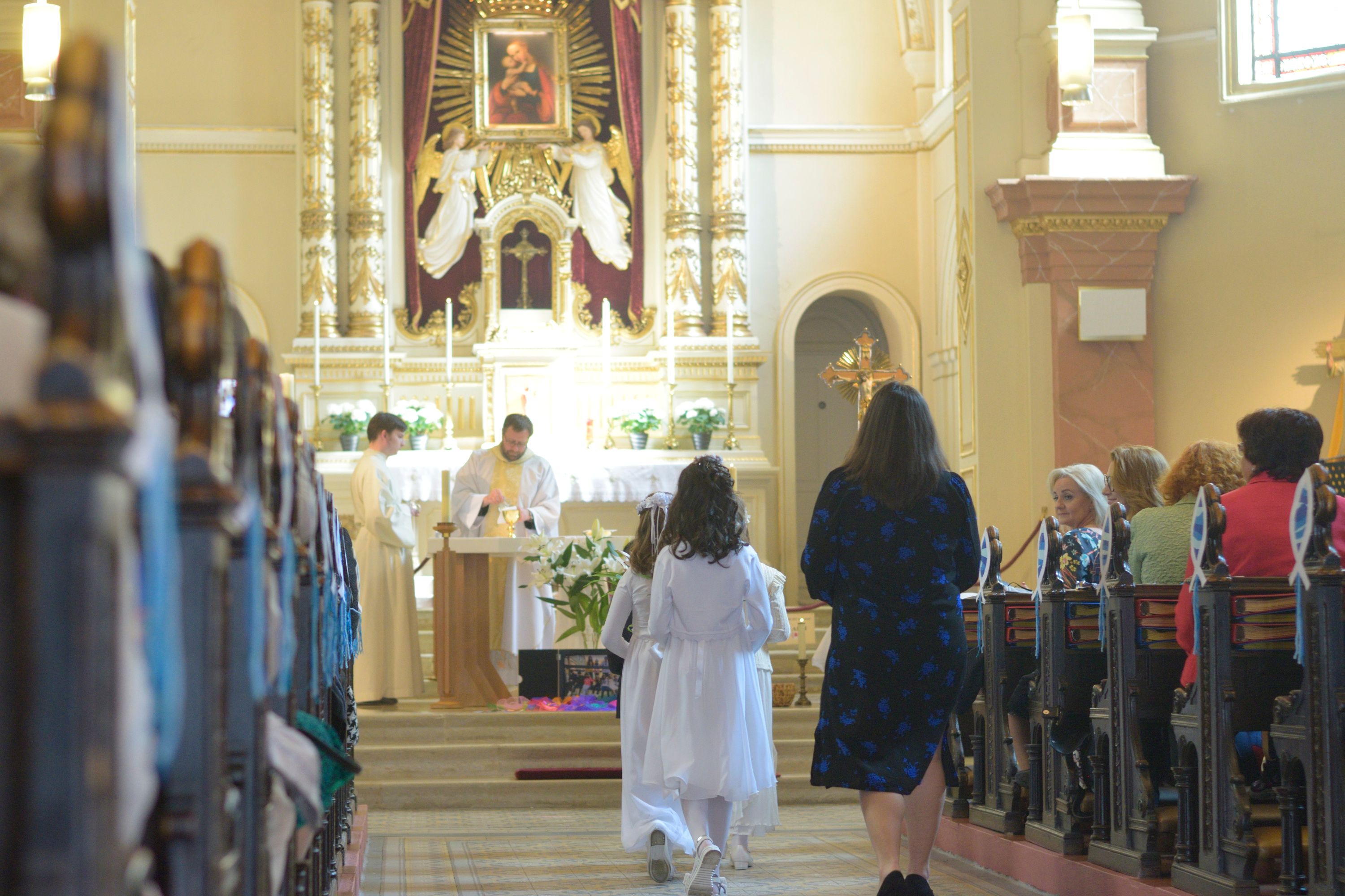 Girls in white dresses walk to the altar during First Communion