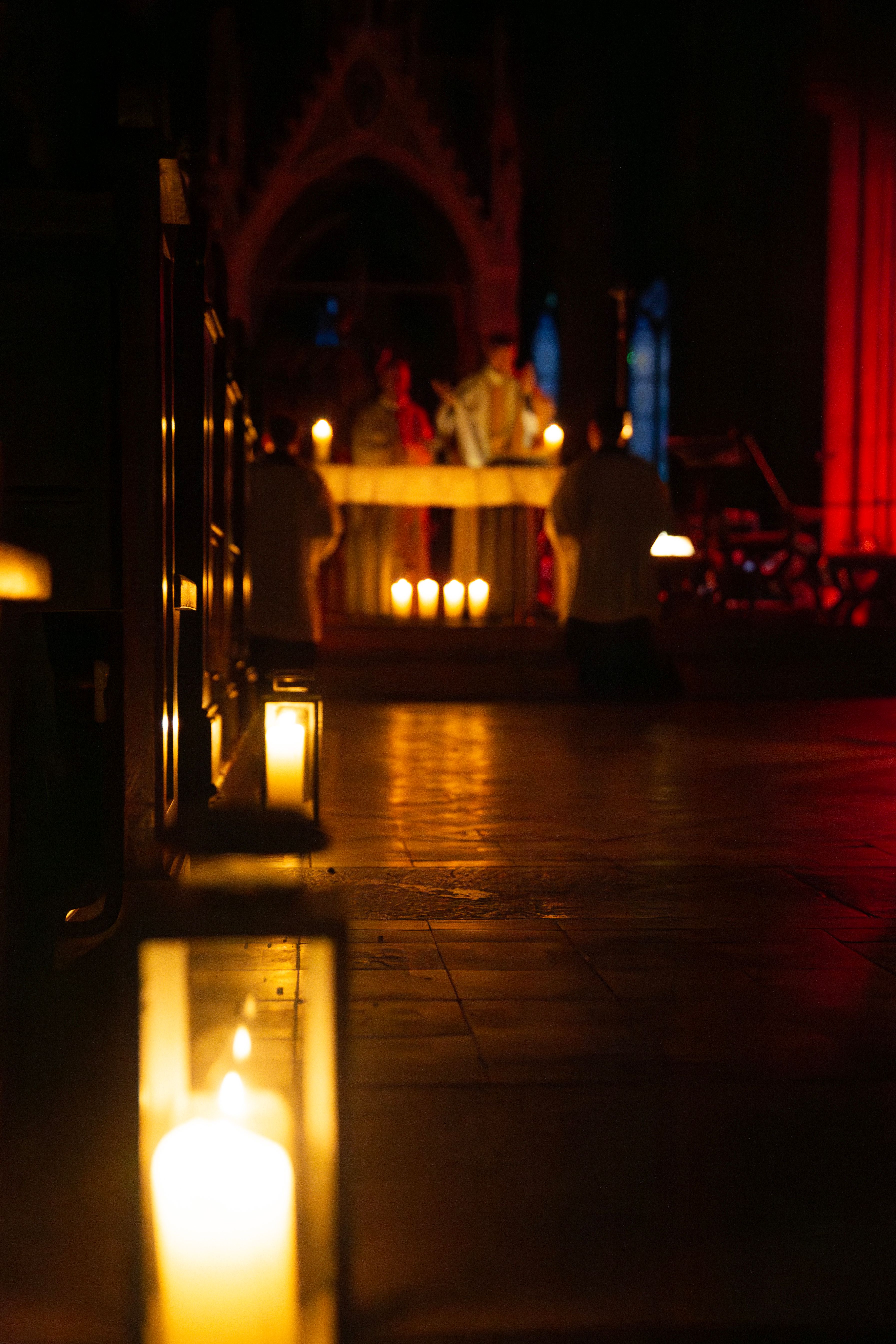 Burning lights in a dark church are placed in the center aisle of a church. Two priests celebrate the Holy Mass in Advent as a Rorate Mass
