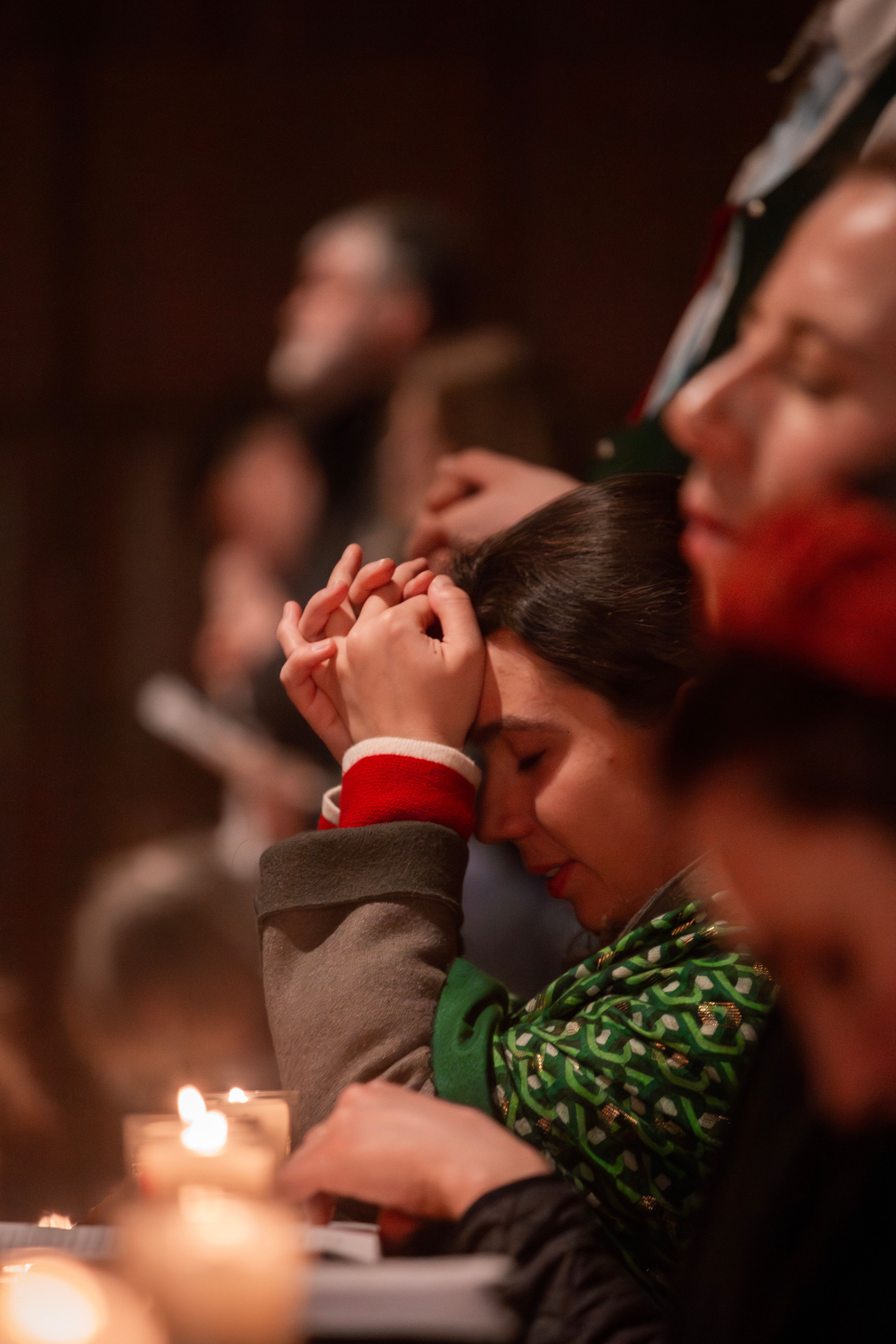 six young people praying; focus of the image is on a woman deep in prayer, candlelight radiates warmth