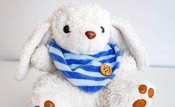 a white rabbit with a blue and white bib (the colors of the radio station Radio Horeb) is sitting in a white room; that rabbit is the mascot of the children's podcast Bamabambini